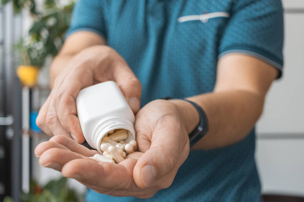 Hombre tomando medicamentos de un frasco, sosteniendo cápsulas terapéuticas blancas, antibióticos, vitaminas, pastillas para el dolor en una mano, vista de cerca. - Foto, Imagen