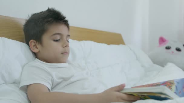 Rapaz giro, livro de leitura infantil na cama. Tiro em câmara lenta média. Imagens 4k de alta qualidade - Filmagem, Vídeo