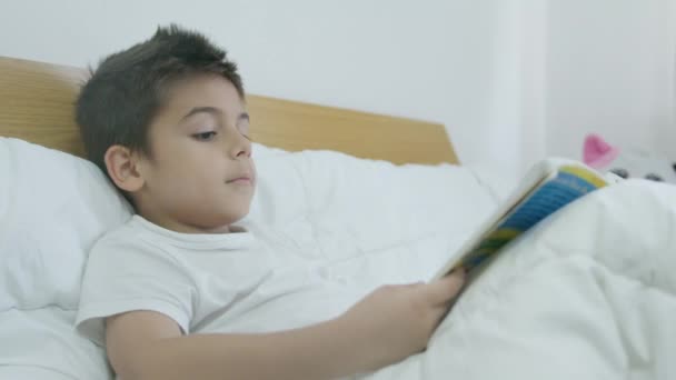 Słodki chłopiec, dziecko czyta książkę w łóżku. Średnio powolne ujęcie. Wysokiej jakości materiał 4k - Materiał filmowy, wideo