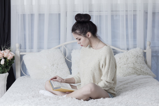 Young woman sitting on the bad at home and reading a book - Foto, afbeelding