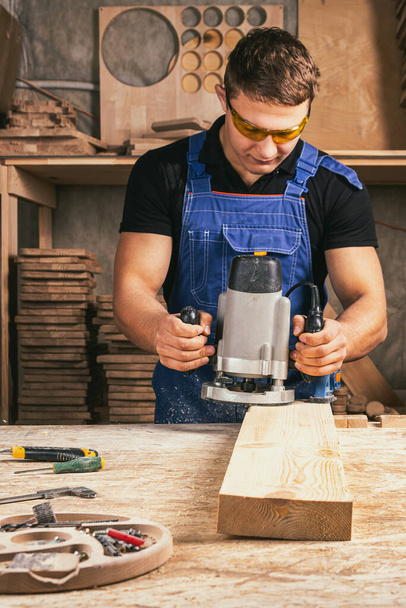 Αρσενικός ξυλουργός που χρησιμοποιεί ηλεκτρικό τριβείο για να γυαλίσει ξύλινη σανίδα σε ξυλουργείο - Φωτογραφία, εικόνα