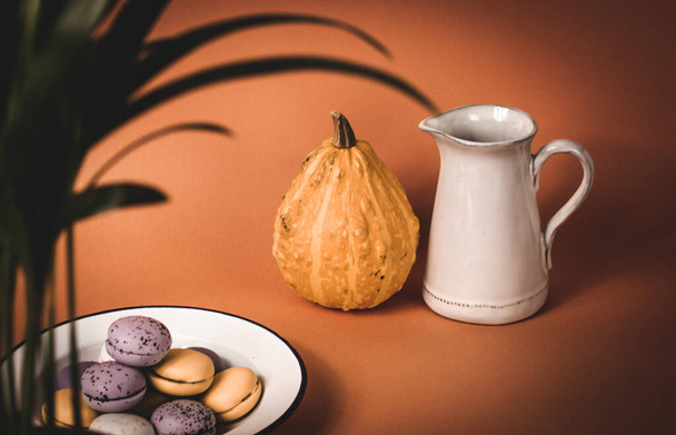 A plate with pumpkin-flavored macaroons. Cooked homemade cookies with rustic recipe. Pastry based on meringue from almond flour. Orange pumpkin in a background. Thanksgiving day table. Vintage photo - Photo, Image