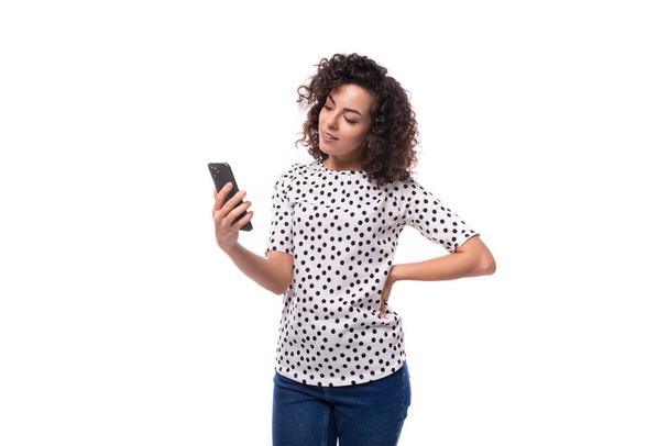 charmant jong brunette krullend vrouw gekleed in de zomer blouse met erwt print chatten op de telefoon. - Foto, afbeelding