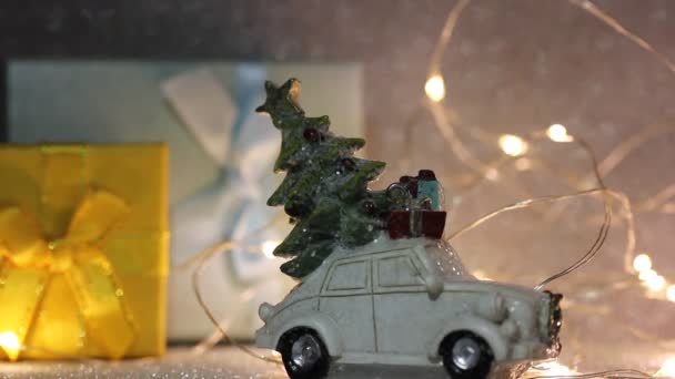 Speelgoed witte retro auto met kerstboom, geschenkdozen op het dak. Nieuwjaar 2024, Kerstconcept. Cadeau kopen, winter winkelen. Cadeaus, slinger gele lichten in de verzilverde glanzende feestelijke achtergrond. - Video