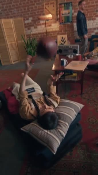 Pionowy uchwyt POV nierozpoznawalnego mężczyzny wykonującego uderzenia pięścią i przybijającego piątkę ze znajomymi podczas nagrywania filmu na kamerę podczas imprezy w studio na poddaszu - Materiał filmowy, wideo