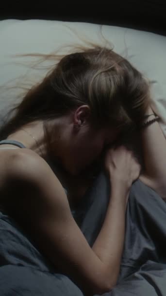 Κάθετη λήψη του κοριτσιού ξαπλωμένη στο κρεβάτι το βράδυ, κρατώντας τα μαλλιά της νευρικά και κλαίγοντας - Πλάνα, βίντεο