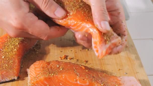 Een stuk verse rode vis wordt bestrooid met specerijen en zout in slow motion van dichtbij bekeken. Zalmsteak op smaak brengen. Chef wrijft de biefstuk met zijn handen voor het bakken. - Video