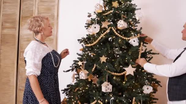 Heureux couple caucasien senior décorer arbre de Noël à la maison, au ralenti. Style de vie des personnes âgées, Noël, célébration et vie familiale, inchangé. - Séquence, vidéo