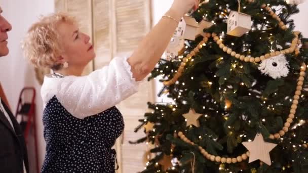 Heureux couple caucasien senior décorer arbre de Noël à la maison, au ralenti. Style de vie des personnes âgées, Noël, célébration et vie familiale, inchangé. - Séquence, vidéo
