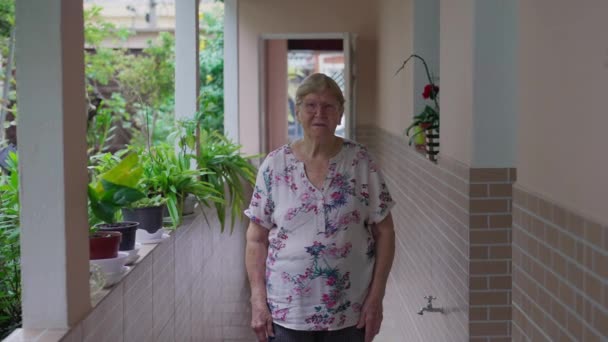 Portret van een oudere vrouw die thuis naar de camera kijkt. Huiselijke levensstijl scène van een volwassen oudere persoon - Video