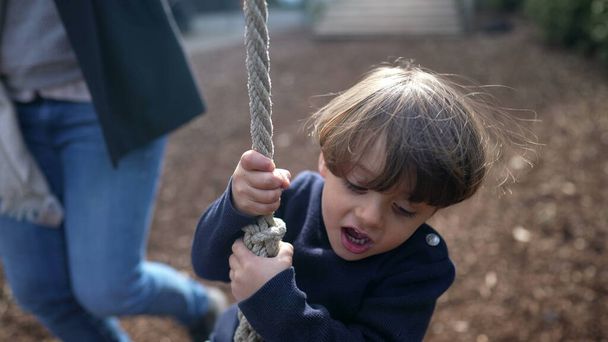 Child Gripping Wire Slide Rope no Parque Público durante a temporada de outono. Encantador Close-Up da criança alegre deslizando na corda de arame entre as árvores, parque nostálgico divertido - Foto, Imagem