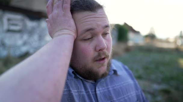 Der Mensch fühlt sich gestresst. Ein frustrierter Übergewichtiger berührt seinen Kopf und hält die Augen geschlossen, wenn er im Freien an Migräne leidet - Filmmaterial, Video
