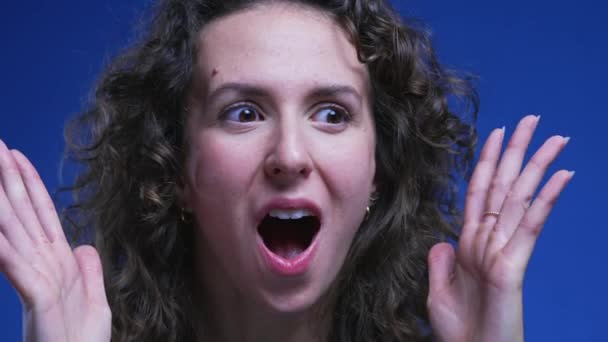 Frau reagiert mit Schock und Überraschung, Gesicht einer erstaunten weiblichen Person in den 20er Jahren, die Erstaunen über Nachrichten auf blauem Hintergrund empfindet - Filmmaterial, Video