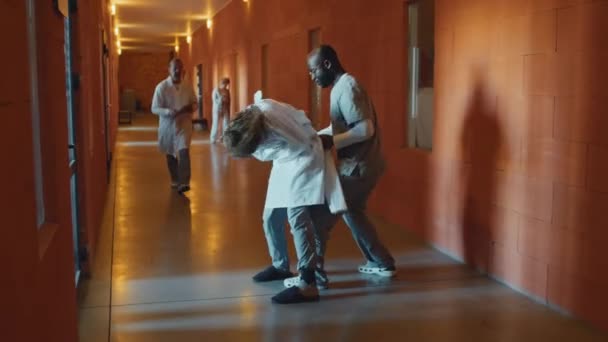 Deux médecins masculins travaillant dans l'asile retenant patient agressif en camisole de force, l'emmenant pour le calmer - Séquence, vidéo