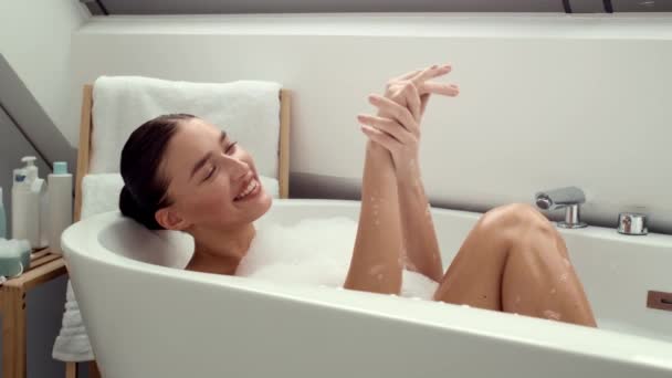 slow motion 4K video footage, a delighted woman is immersed in foam-filled bath, gently washing her hands and playfully engaging with the bubbles. The scene is a blend of relaxation and childlike joy - Footage, Video