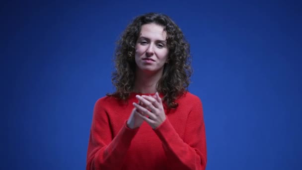 Young woman applauding viewer and pointing finger acknowledging successful achievement. 20s female person congratulating standing on blue backdrop - Footage, Video