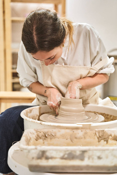 Художня жінка формує глину на керамічному колесі, працюючи у своїй майстерні. концепція хобі та ремесел. - Фото, зображення