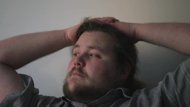 Egy töprengő, fiatal, túlsúlyos férfi közelít az arcához elmélkedés közben. Egy kövér fickó portréja, aki az életre gondol. Átgondolt érzelem. - Felvétel, videó
