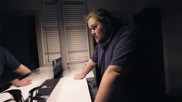 Ένας απελπισμένος υπέρβαρος άντρας στέκεται μπροστά στον καθρέφτη του μπάνιου κοιτάζοντας την αντανάκλασή του στην απελπισία. - Πλάνα, βίντεο