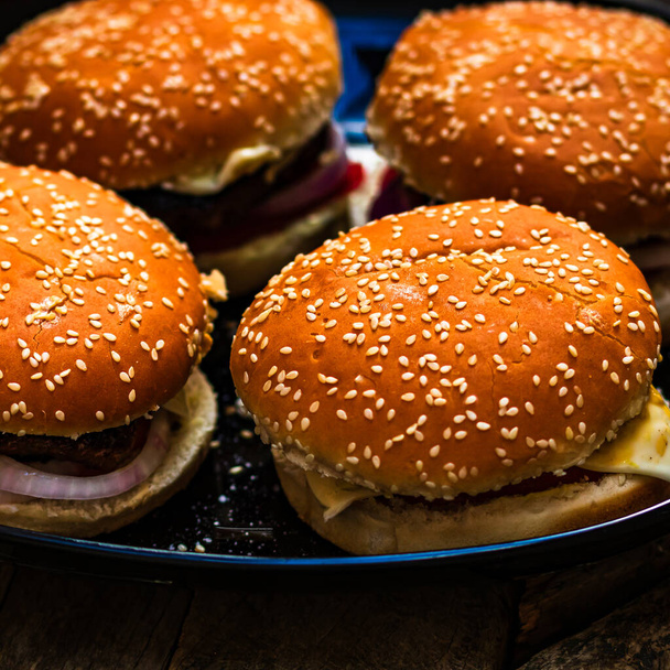 Leckere hausgemachte Cheeseburger. Käseburger mit Essiggurken, Tomaten, Zwiebeln, schmelzendem Käse - Foto, Bild