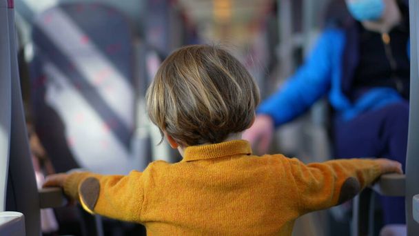 Μικρό αγόρι που στέκεται στο διάδρομο του τρένου και κρατιέται σε καθίσματα. Παιδί περνά την ώρα του στις σιδηροδρομικές μεταφορές φορώντας κίτρινα ρούχα και μπότες - Φωτογραφία, εικόνα