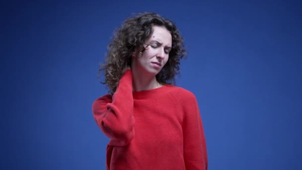 Vrouw die nekpijn voelt hand op hand worstelend met lichaamspijn staand op blauwe achtergrond - Video