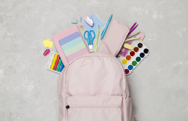 Pinkfarbener Schulrucksack mit Papeterie auf Betonhintergrund, Draufsicht - Foto, Bild