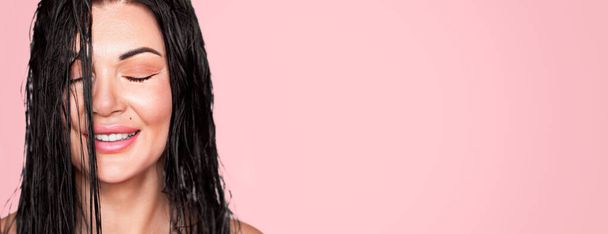 Beautiful girl, woman with dark wet hair. Smiling. Closed eyes. Close-up on a pink background. - Photo, Image