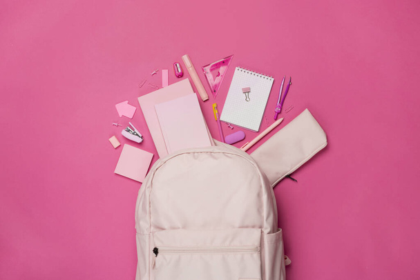 Рюкзак розовой школы с канцелярскими принадлежностями на цветном фоне, вид сверху - Фото, изображение
