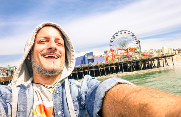 Όμορφος άνδρας λαμβάνοντας μια selfie στην Santa Monica προβλήτα με ρόδα - ηλιόλουστη μέρα στην Καλιφόρνια ακτή - περιπέτεια ταξίδι τρόπου ζωής γύρω από τις Ηνωμένες Πολιτείες της Αμερικής - σύνθεση με κλίση ορίζοντα - Φωτογραφία, εικόνα