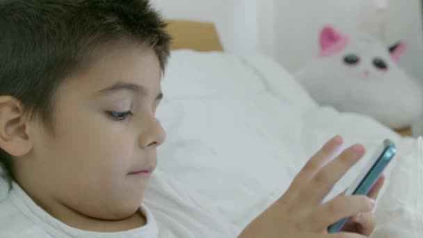 Mignon garçon caucasien couché dans le lit et regarder des dessins animés au téléphone. Images 4k de haute qualité - Séquence, vidéo