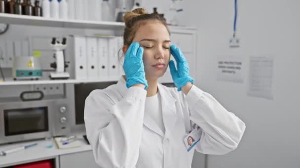 Stressato giovane donna ispanica in uniforme scienziato che soffre di un mal di testa doloroso emicrania in laboratorio - Filmati, video