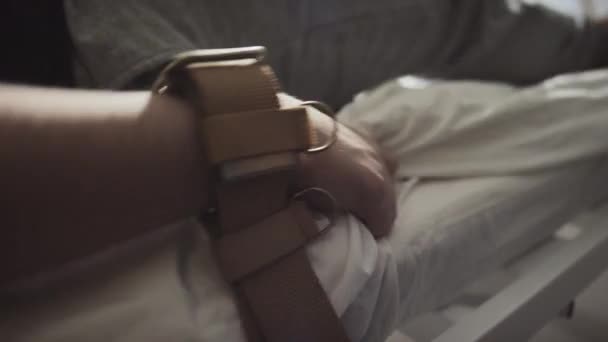 Enfoque selectivo de un paciente irreconocible con enfermedad mental con brazos atados a la cama del hospital con cinturones marrones que sufren convulsiones - Metraje, vídeo