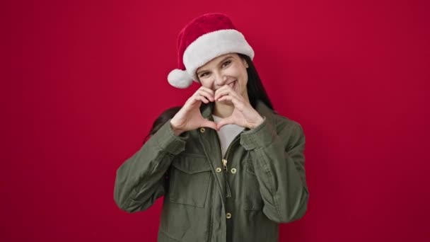 Молода красива іспаномовна жінка в Різдво робить жест серця над ізольованим червоним тлом - Кадри, відео