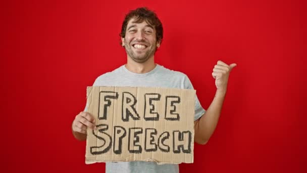 Fröhlicher junger Mann, Banner in der Hand, Daumen hoch und strahlendes Lächeln, zelebriert freie Meinungsäußerung vor auffallend rotem Hintergrund - Filmmaterial, Video