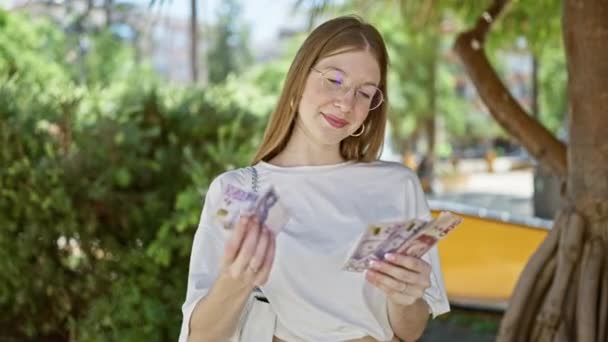 Jonge blonde vrouw lacht zelfverzekerd tellen Zweedse kroon bankbiljetten in het park - Video
