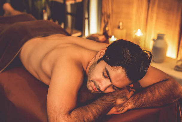 Cliente uomo caucasico godendo rilassante massaggio spa anti-stress e coccole con la bellezza svago della pelle in calda illuminazione a candela ambiente salone spa presso resort di lusso o hotel. Silenzioso - Foto, immagini