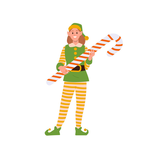 Счастливая улыбающаяся девочка эльф персонаж мультфильма Санта-Клаус помощник держа конфетку сладкий вкусный десерт векторную иллюстрацию. Улыбающийся детский персонаж в зеленом костюме, держащий огромное рождественское угощение - Вектор,изображение