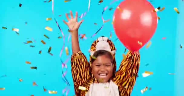 Komik, kaplan kostümü ve çocuğun yüzü balonlarla, konfetilerle ve mavi bir arka plan modelleme alanında izole edilmiş bir şekilde kutlanıyor. Portre, doğum günü partisi ve hayvan kostümüyle gülen mutlu kız.. - Video, Çekim