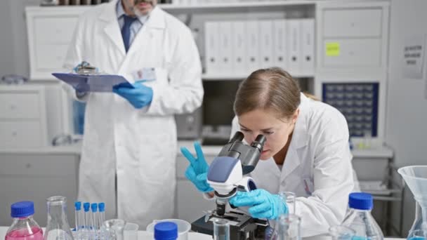 Két komoly tudós jegyzetel és mikroszkópot használ a laborban, egy férfi és egy nő együtt dolgoznak intenzív kutatásban a beltéri laboratóriumban. - Felvétel, videó