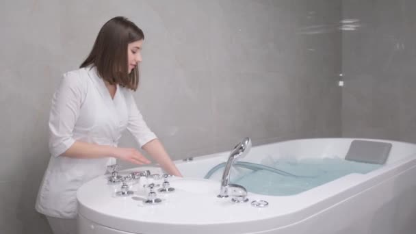 女性のスパの専門家は,ハイドロマッサージ手順のための湯でバスタブを満たしています. プロのハイドロマッサージ. - 映像、動画