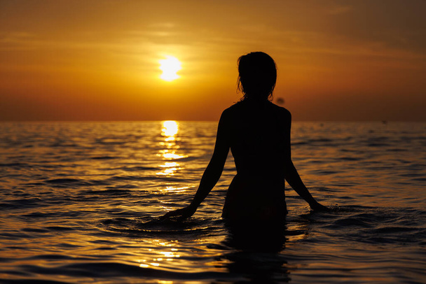 Silhouette d'une fille dans la mer vous regarde au coucher du soleil. - Photo, image