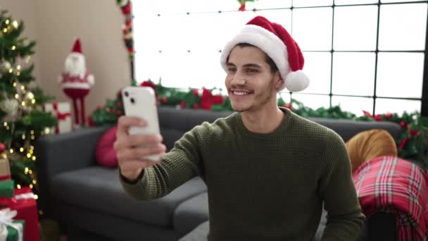 Νεαρός ισπανόφωνος άνδρας που έχει βιντεοκλήση κάθεται στον καναπέ δίπλα στο χριστουγεννιάτικο δέντρο στο σπίτι - Πλάνα, βίντεο