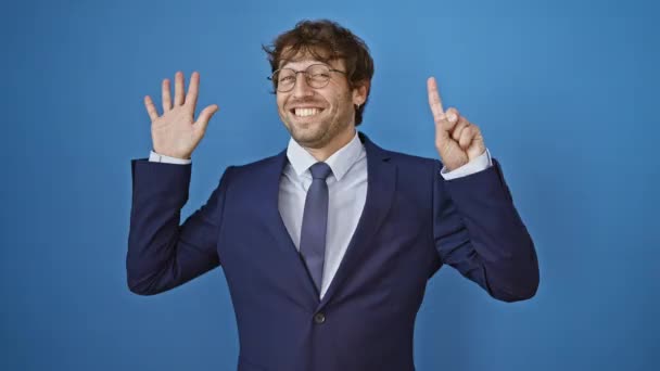 Giovane uomo in giacca e cravatta mostrando e indicando con le dita il numero sei, sorridendo fiducioso e felice. su sfondo blu isolato - Filmati, video