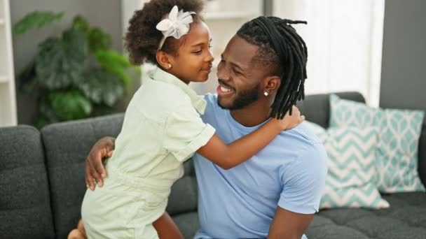 Afrykański amerykański ojciec i córka uśmiecha się pewnie przytulając się siedząc na kanapie w domu - Materiał filmowy, wideo