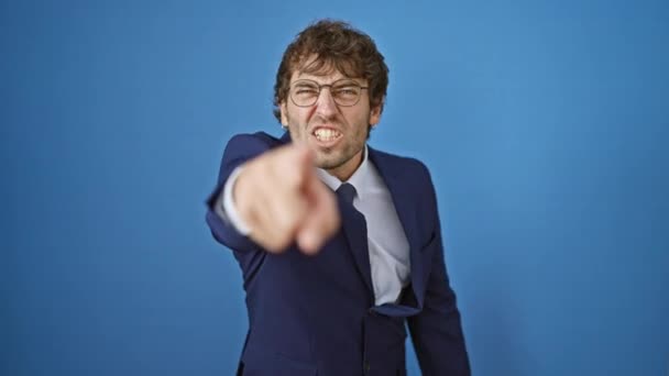Furious, young man in a business suit, angrily pointing at you in a displeased fit, captured on camera against an isolated blue background. - Footage, Video