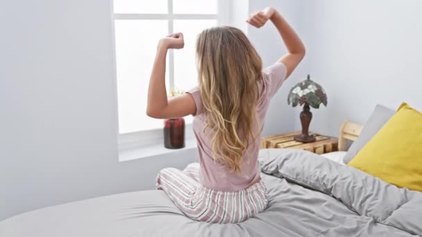 Prachtige jonge blonde vrouw genieten van een ochtend stretch, wakker worden in het comfort van haar gezellige slaapkamer, het gevoel van de ontspanning wassen over haar - Video