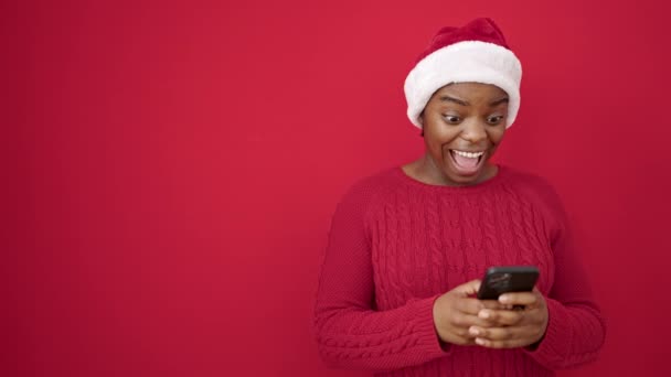 Afrikaans amerikaanse vrouw het dragen van kerst hoed met behulp van smartphone over geïsoleerde rode achtergrond - Video