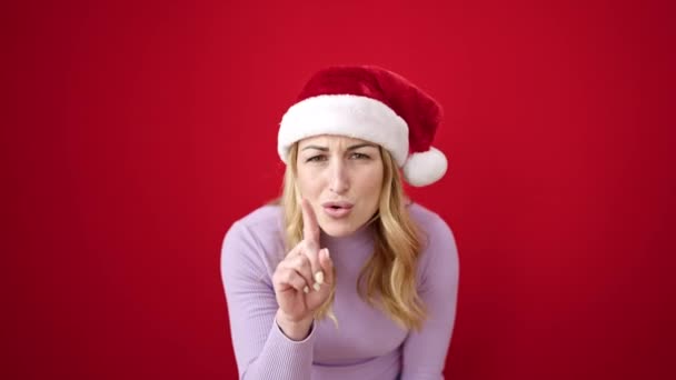 Νεαρή όμορφη ισπανόφωνη γυναίκα στέκεται με σοβαρή έκφραση φορώντας χριστουγεννιάτικο καπέλο λέγοντας όχι με το δάχτυλο πάνω από απομονωμένο κόκκινο φόντο - Πλάνα, βίντεο