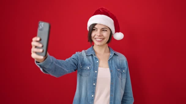 jonge Kaukasische vrouw het nemen van een selfie foto dragen van kerst hoed over geïsoleerde rode achtergrond - Video